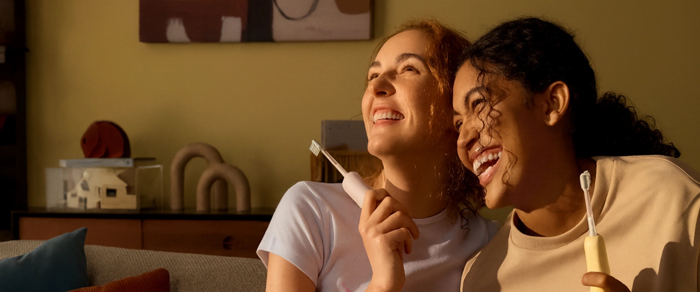 Two women sitting together, holding and looking at the electirc toothbrush in a cozy living room.